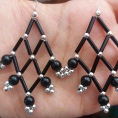 two pairs of black beaded earrings are held in someone's hand with their fingers