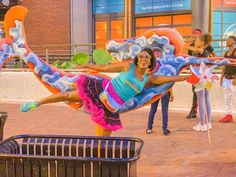 a woman in a colorful costume is doing a trick on the street while others watch