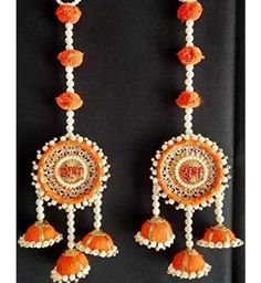 two orange and white earrings hanging from a black wall with beads on it's sides