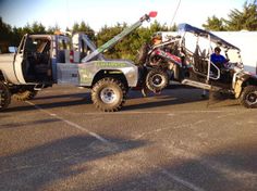 two trucks parked in a parking lot with one being lifted off the ground by another