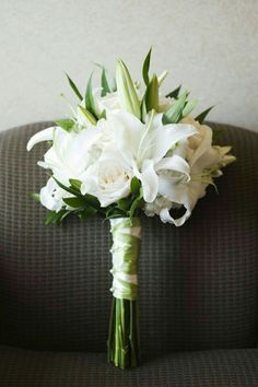 a bouquet of white flowers sitting on top of a gray couch next to a wall