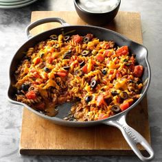 a skillet filled with taco and beans on top of a wooden cutting board