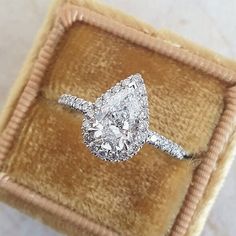 an engagement ring with a pear shaped diamond on top in a velvet box that is sitting on a marble surface