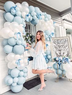 a woman standing in front of a blue and white balloon arch