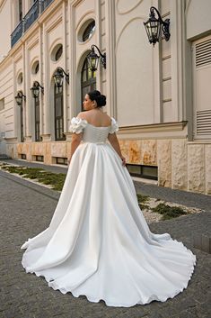 a woman in a white wedding dress is standing on the side walk looking off into the distance