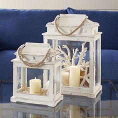 two white lanterns with candles are sitting on a glass table in front of a blue couch