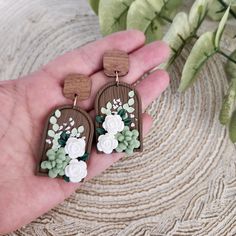 a pair of wooden earrings with white flowers on them sitting in someone's hand