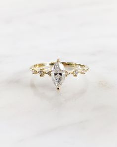 a white and yellow gold ring with a pear shaped diamond in the center on a marble surface