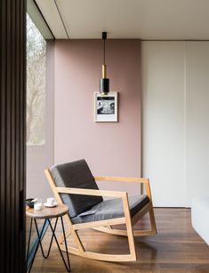 a modern rocking chair in the corner of a room with pink walls and wood flooring