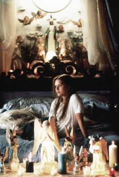 a woman sitting on top of a bed surrounded by figurines and candle lights