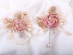 two brooches with flowers and pearls are on a white fabric background, one is pink