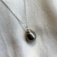 "A stunning dark grey Tahitian pearl pendant on a sparkling sterling silver chain.  * 14mm x 12mm natural black / grey Tahitian pearl * 18\" / 45cm sterling silver diamond cut chain * bolt ring clasp * minimalist design  This stunning Tahitian pearl has the most gorgeous silver grey sheen with a soft pink glow at the top of the teardrop shaped pearl. The sparkling diamond cut chain finishes with a 5mm bolt ring style clasp. With its fabulous size and gorgeous colour this pearl necklace makes a h Silver Tahitian Pearl Necklace With High Luster, Gray Pearl Drop Jewelry For Gift, Silver Tahitian Pearl Necklace With Pearl Charm, Silver Tahitian Pearl Necklace With Pearl Drop, Tahitian Pearl Round Pendant Necklace For Anniversary, Tahitian Pearl Pendant Jewelry As Gift, Black Pearl Necklace With High Luster For Gift, White Gold Tahitian Pearl Necklace For Gift, Gray Sterling Silver Necklace For Gift