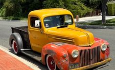 an old yellow truck is parked on the side of the road