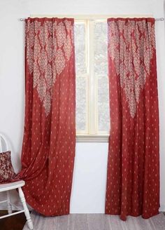 a red curtain hanging in front of a window next to a white chair with a pillow on it