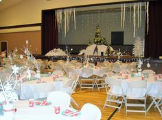 tables and chairs are set up for an event with white tablecloths, snowflakes, and decorations