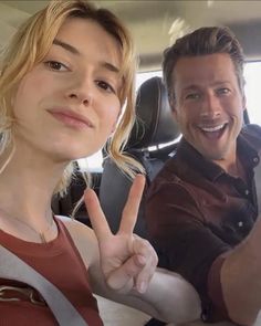 a man and woman sitting in a car giving the peace sign