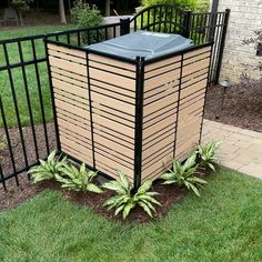 a trash can sitting in the grass next to a fence and some plants on the ground