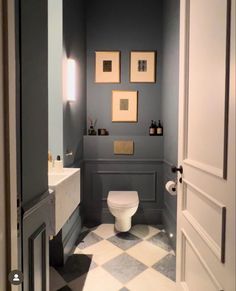 a white toilet sitting inside of a bathroom next to a sink and mirror with pictures on the wall