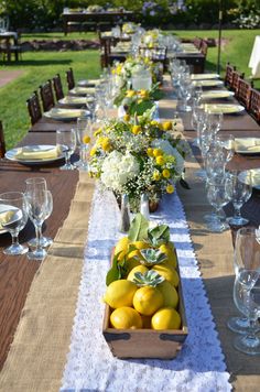 a long table is set with lemons and white flowers in a wooden box on top