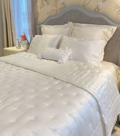 a bed with white comforters and pillows in a bedroom