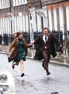 a man and woman running down the street in the rain with an old car behind them