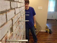 a man standing next to a brick wall holding a screwdriver in his hand