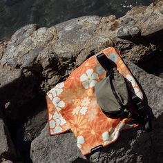 an orange and white flowered bag sitting on rocks next to the ocean with water in the background