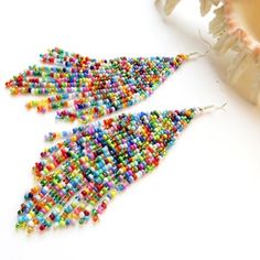 two pairs of colorful beaded earrings sitting on top of a white table next to flowers