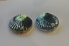 two silver shell shaped objects sitting on top of a white countertop next to each other