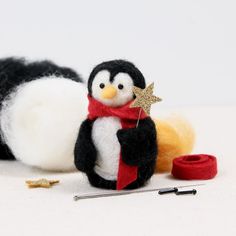 a small penguin with a scarf and star on its nose next to some knitting needles