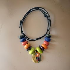 This handcrafted ceramic jewelry is a one-of-a-kind masterpiece featuring a handmade and hand-painted abstract pendant. The pendant is approximately 20mm x 30mm. Complemented by handmade porcelain beads in vibrant tangerine orange, forest and lime green, fuchsia, peacock shades of blue and green, it exudes unique charm. Enhanced with luxurious real leather cording, each piece is meticulously crafted to last. Every boho necklace is strung with an adjustable knot for a perfect fit (length approximately 18" to 24"). Please cherish the slight imperfections that add to the allure of these fragile, one-of-a-kind creations, each radiating its own distinct beauty. What makes this handmade pendant necklace unique? This boho necklace is a one-of-a-kind masterpiece, featuring a handmade and hand-pain Everyday Multicolor Resin Jewelry, Hand Painted Artisan Jewelry For Everyday, Artisan Hand Painted Everyday Jewelry, Artsy Multicolor Round Pendant Necklace, Everyday Artisan Hand Painted Jewelry, Artsy Multicolor Round Pendant Jewelry, Large Beads Polymer Clay Jewelry As A Gift, Colorful Beads Polymer Clay Necklace Gift, Colorful Beads Polymer Clay Necklace For Gift