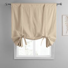 a window with a beige curtain and bow tie - up on the valance, in front of a white wall