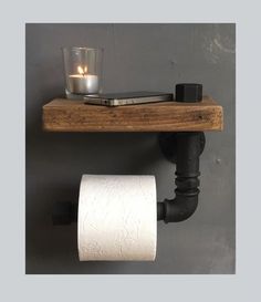 a toilet paper holder with a phone on it and a candle next to it in front of a gray wall