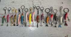 many different types of fishing lures hanging on a white wooden wall with keychains