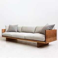 a wooden couch with pillows on it in front of a white wall and concrete floor