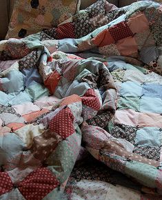 an unmade bed is covered with colorful quilts on the floor next to a window