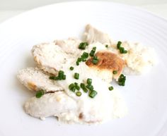 a white plate topped with chicken covered in gravy and green onion garnish