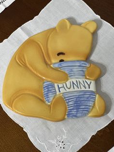 a ceramic bear holding a blue cup on top of a white doily with the word hummy