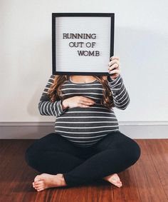 a pregnant woman sitting on the floor holding up a sign that says running out of women