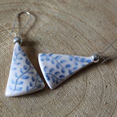 two blue and white ceramic earrings hanging from silver hooks on a piece of cloth covered surface