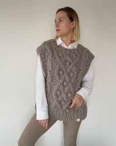 a woman standing in front of a white wall wearing a sweater and leggings