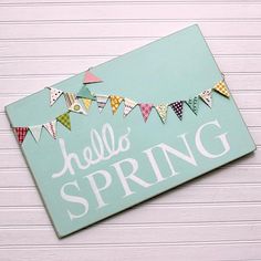 a sign that says hello spring hanging on the side of a white wall with bunting