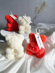 three small teddy bears with tags on them sitting on a white cloth covered tablecloth