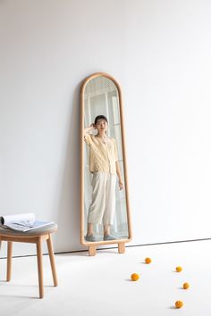 a woman standing in front of a mirror with oranges on the floor next to it