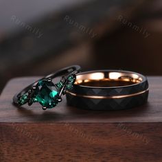 two wedding rings with green stones on them sitting on top of a wooden table next to each other