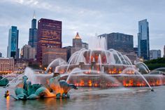 the fountains are lit up in front of the city skyline