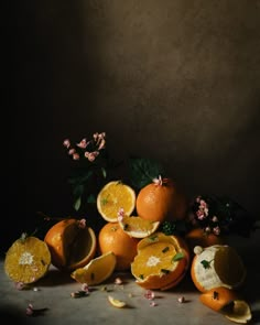 an arrangement of oranges with leaves and flowers on a dark background, in front of a gray wall