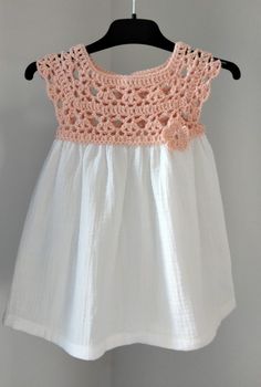 a white dress with pink crochet on the top and bottom, hanging from a hanger