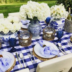 a blue and white table setting with flowers in vases, plates, napkins and utensils