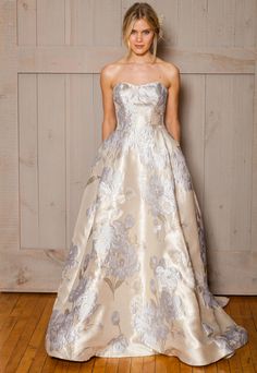 a woman standing in front of a wooden wall wearing a dress with flowers on it